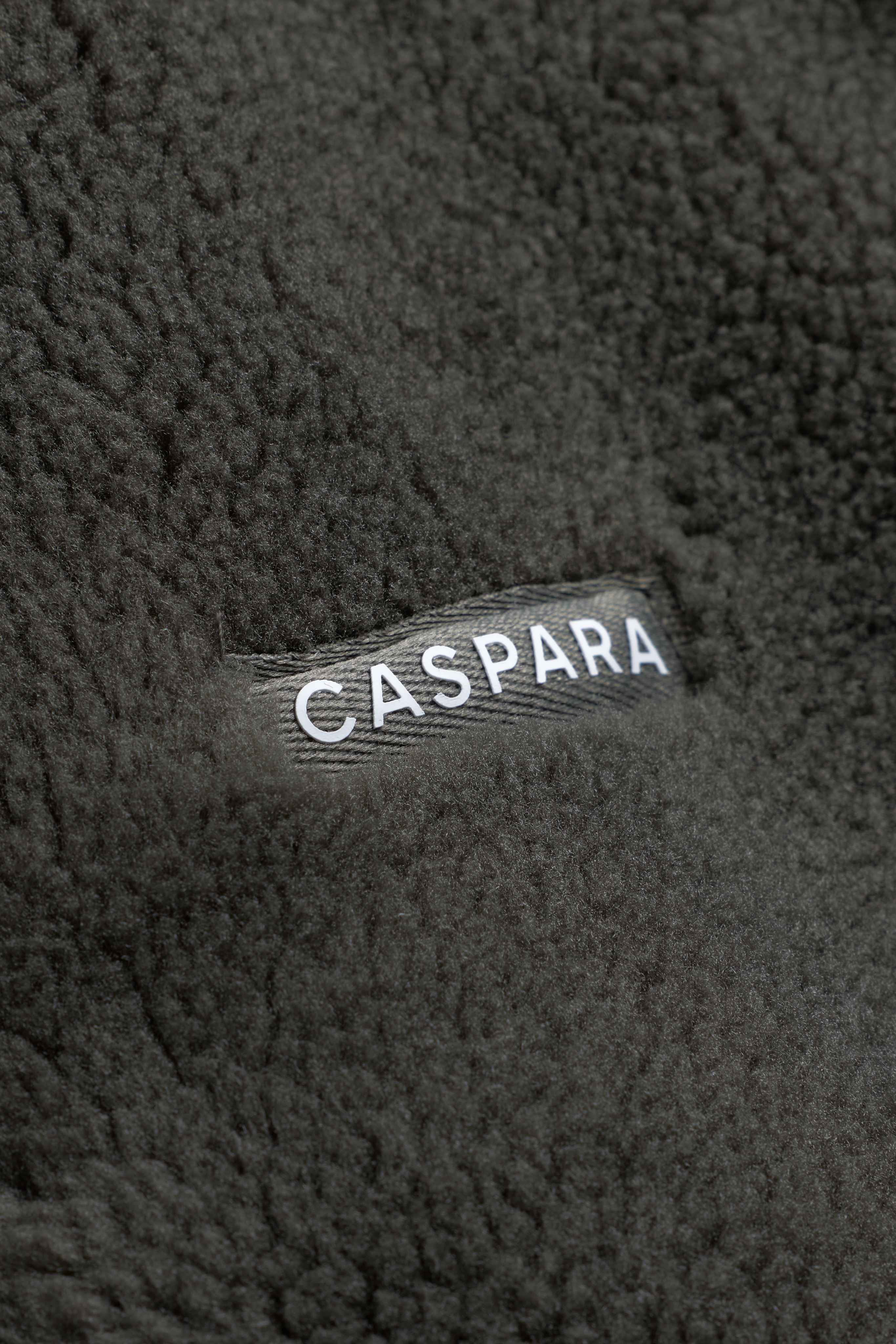 Close-up of the khaki fleece texture on the CASPARA Cloudfleece vest, featuring a woven logo label.